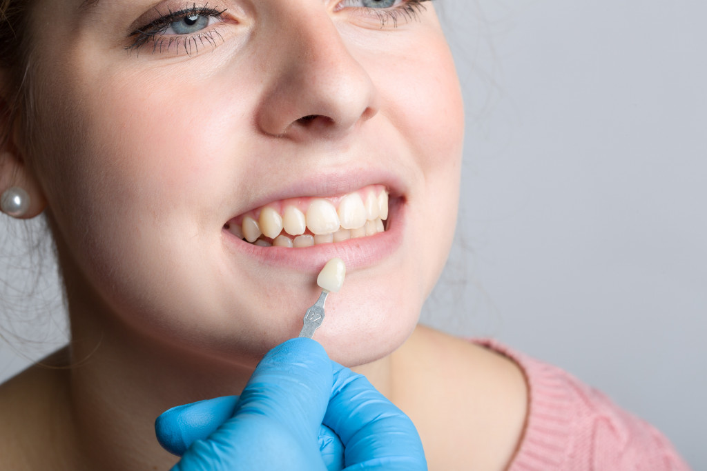 woman smiling with her teeth compared to a veneer held by gloved dentist