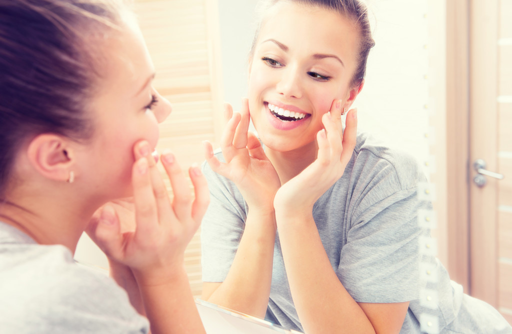 A young woman touching her face in front of a mirror